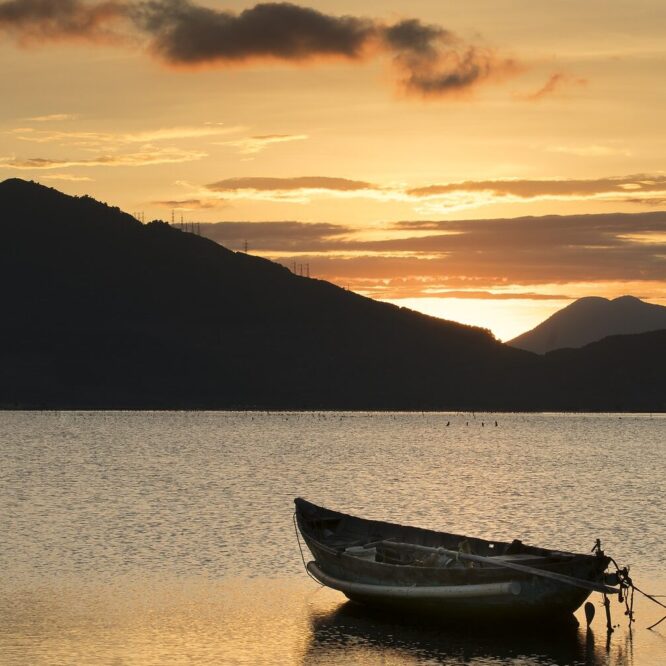 A boat on calm water at sunset with hills in the background.