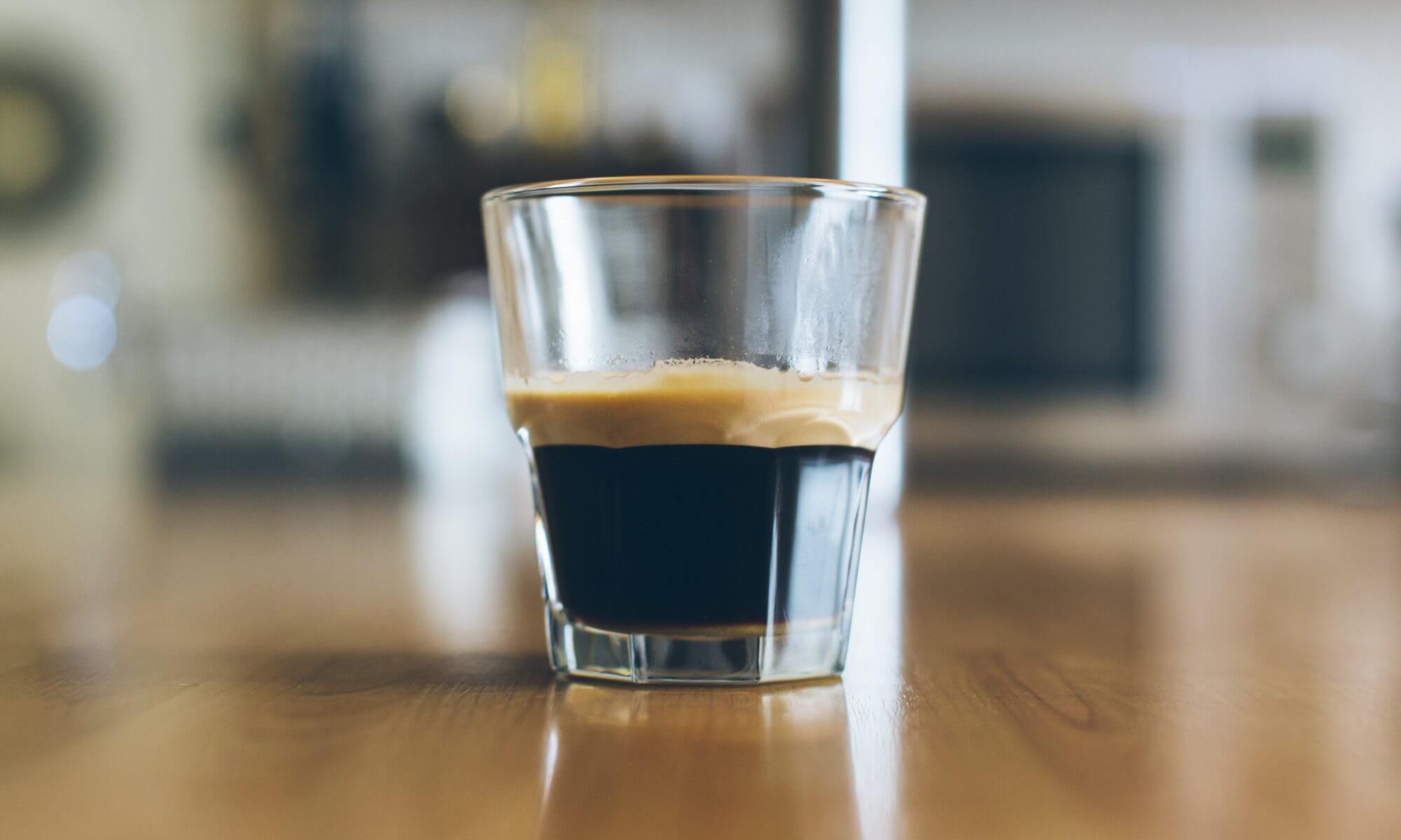 A small glass of espresso on a wooden table.