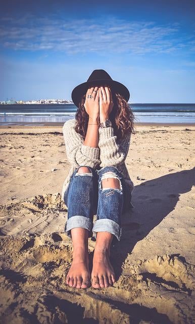 A woman sitting on the beach covering her face with her hands.